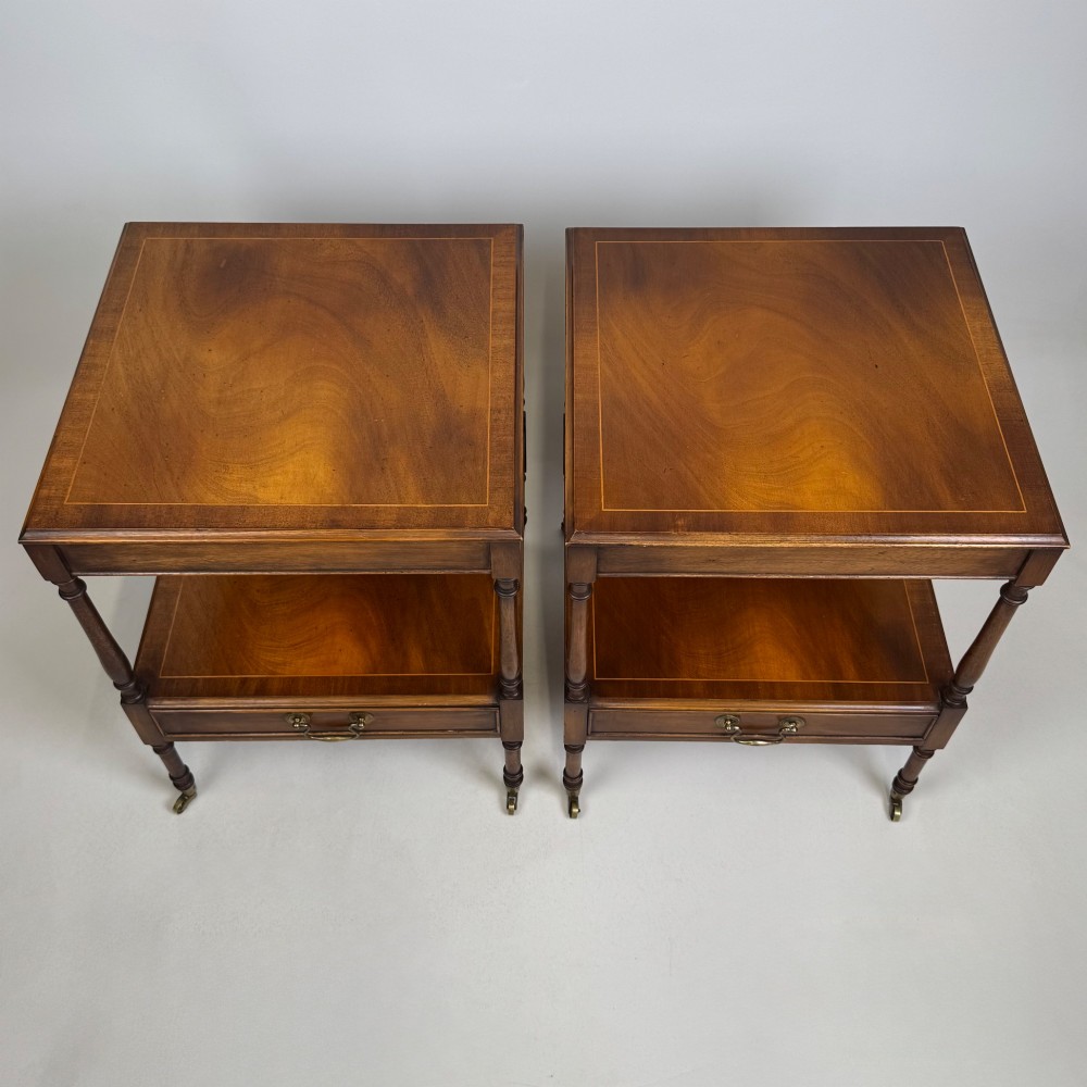 A pair of 20th-century warm mahogany bedside tables featuring turned support pillars, open middle shelves, single lower drawers with brass handles, and brass castors. View XII