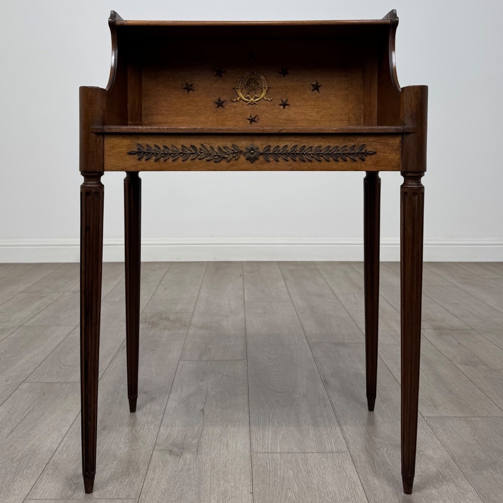 A French mahogany side table featuring slim tapered fluted legs, a carved laurel motif apron, and a gallery back adorned with brass stars.