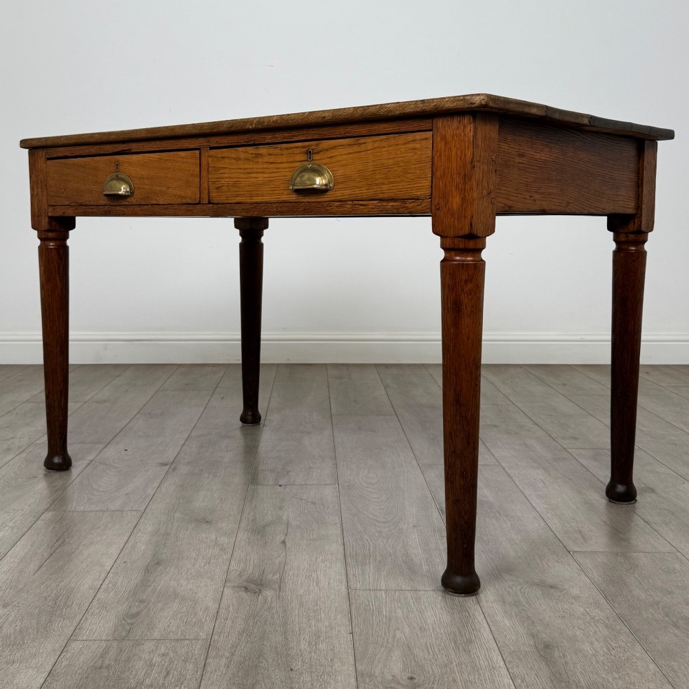 An antique early 20th-century oak writing table featuring two front drawers with brass cup handles and turned legs. View II