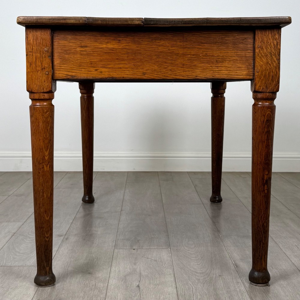 An antique early 20th-century oak writing table featuring two front drawers with brass cup handles and turned legs. View III