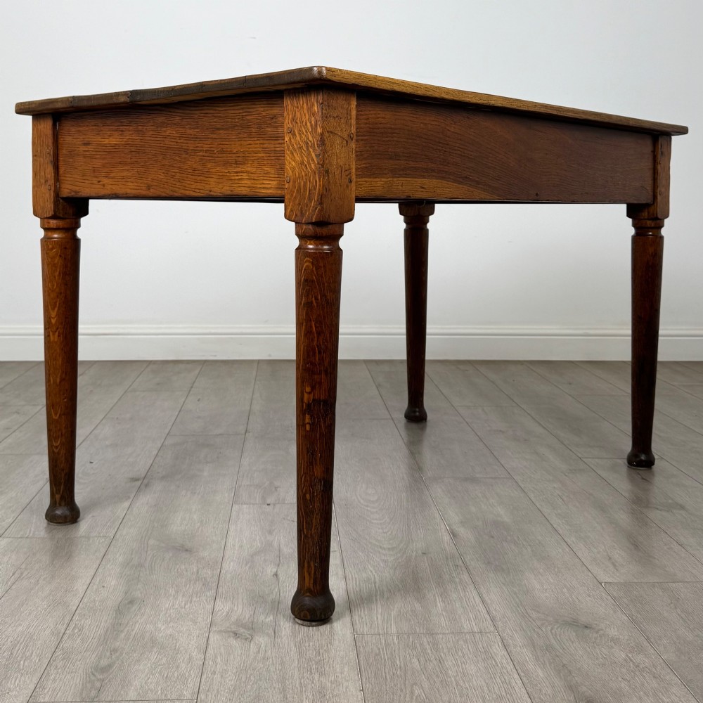 An antique early 20th-century oak writing table featuring two front drawers with brass cup handles and turned legs. View IV