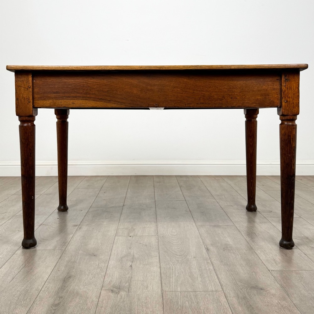 An antique early 20th-century oak writing table featuring two front drawers with brass cup handles and turned legs. View V