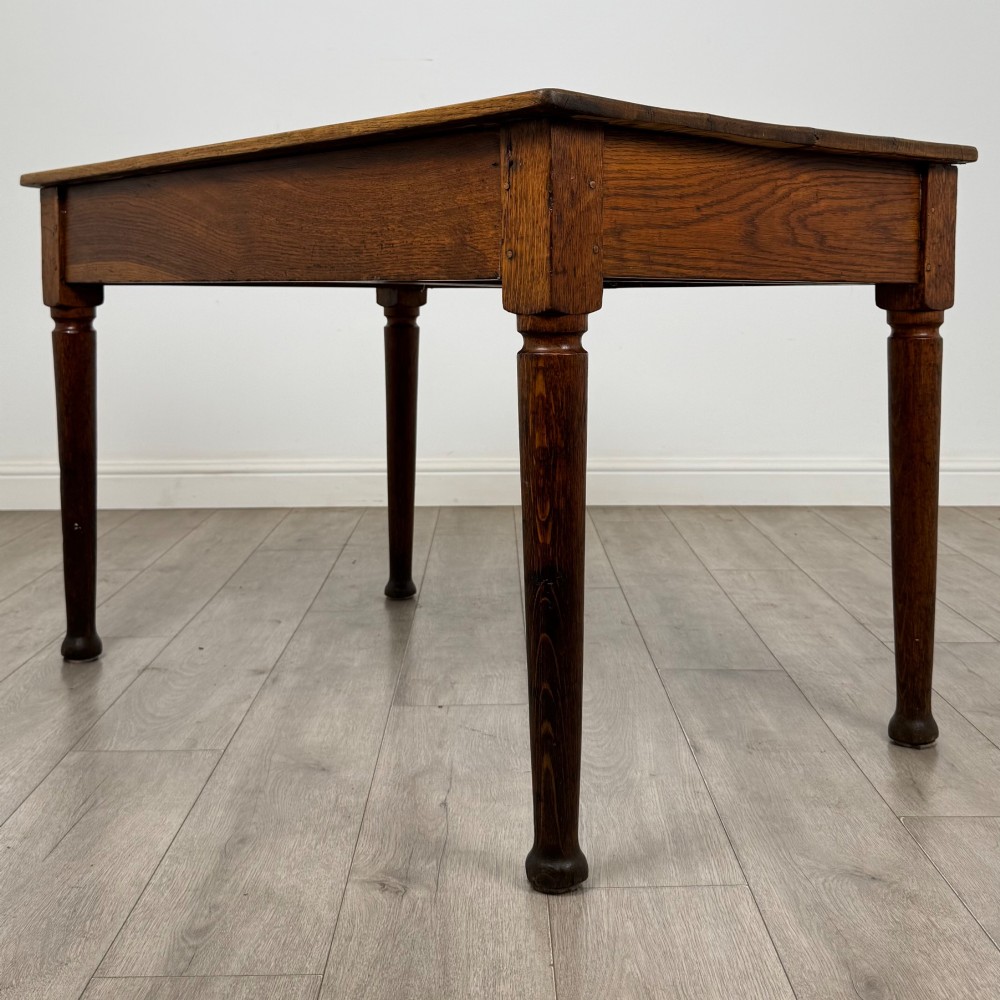 An antique early 20th-century oak writing table featuring two front drawers with brass cup handles and turned legs. View VI