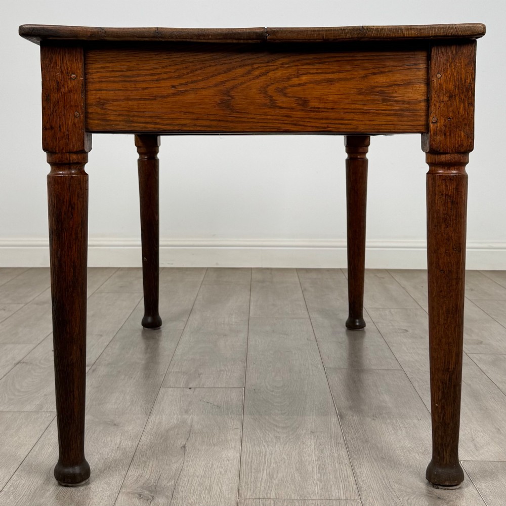 An antique early 20th-century oak writing table featuring two front drawers with brass cup handles and turned legs. View VII