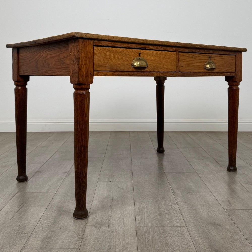 An antique early 20th-century oak writing table featuring two front drawers with brass cup handles and turned legs. View VIII