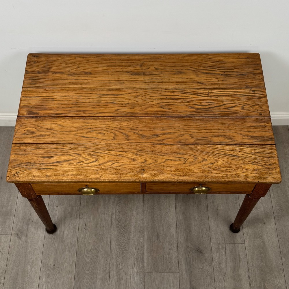 An antique early 20th-century oak writing table featuring two front drawers with brass cup handles and turned legs. View IX