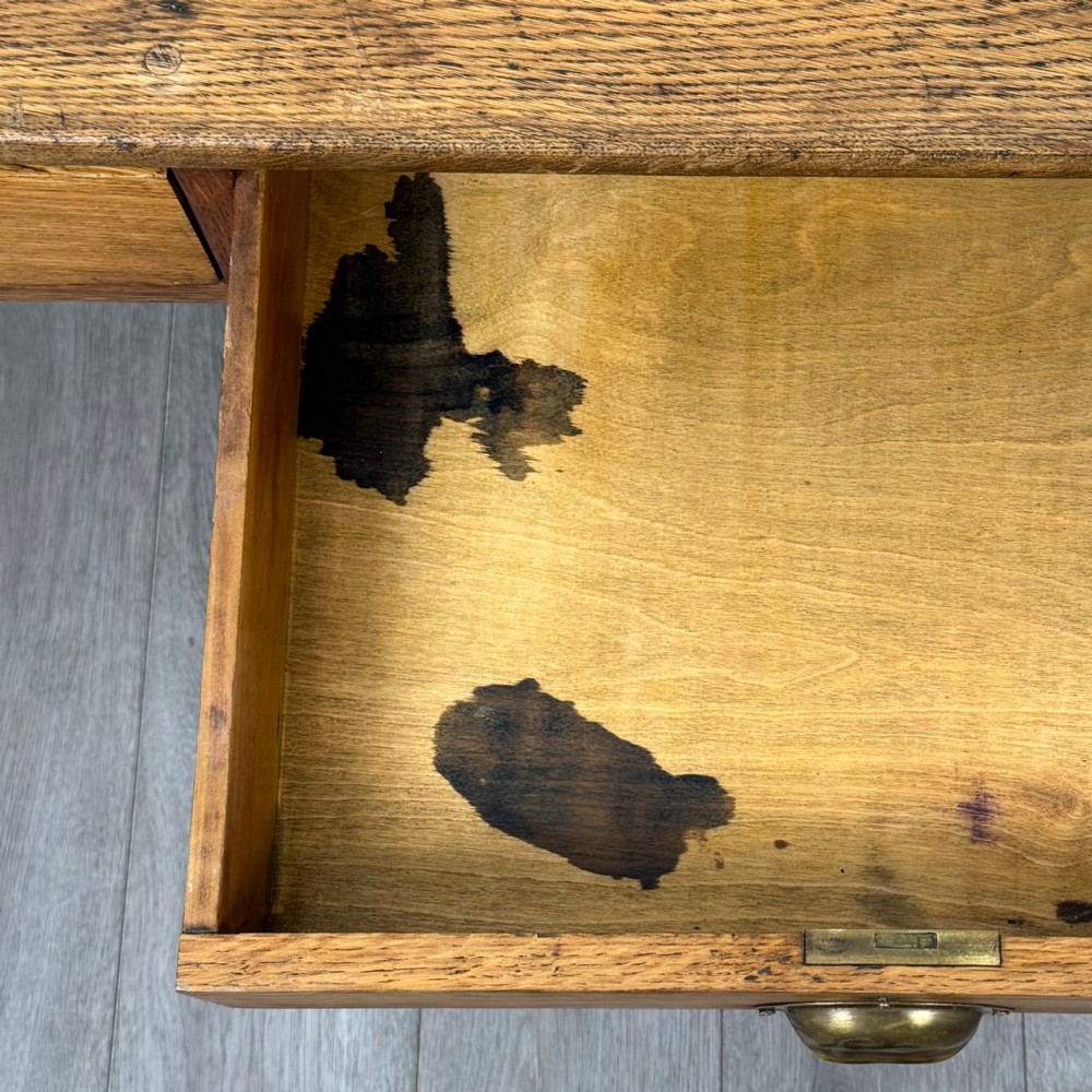 An antique early 20th-century oak writing table featuring two front drawers with brass cup handles and turned legs. View XII
