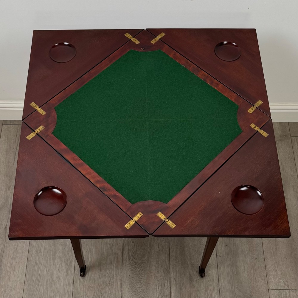 An Edwardian mahogany envelope card table with crossbanded satinwood inlay, a single drawer, and tapered square legs on brass castors. View XI