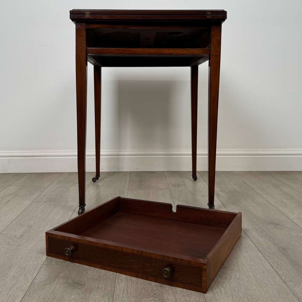 An Edwardian mahogany envelope card table with crossbanded satinwood inlay, a single drawer, and tapered square legs on brass castors. View XII