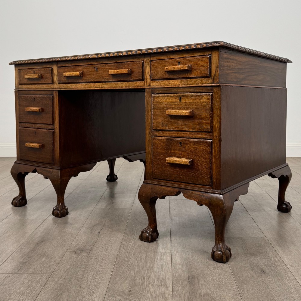 An antique oak pedestal desk featuring twin drawer pedestals, carved borders, and cabriole legs terminating in ball-and-claw feet. View II