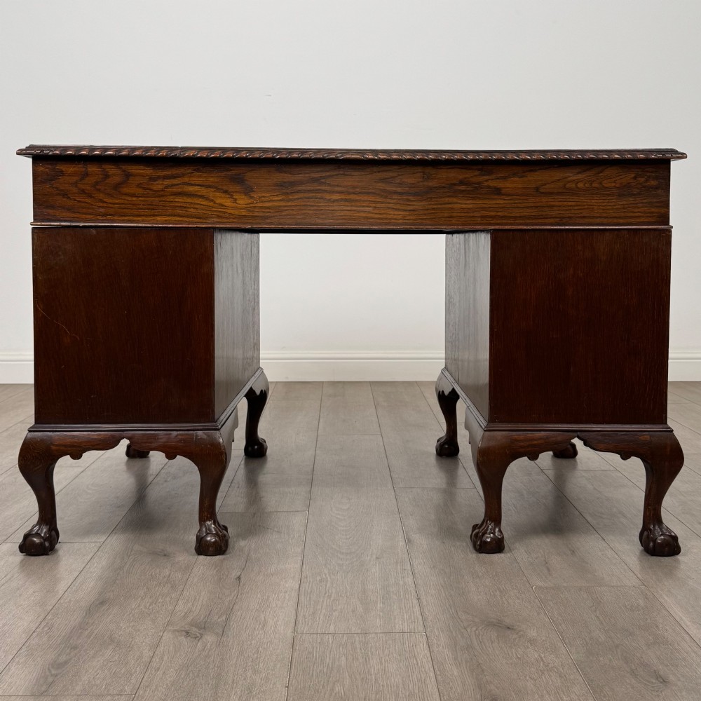 An antique oak pedestal desk featuring twin drawer pedestals, carved borders, and cabriole legs terminating in ball-and-claw feet. View V