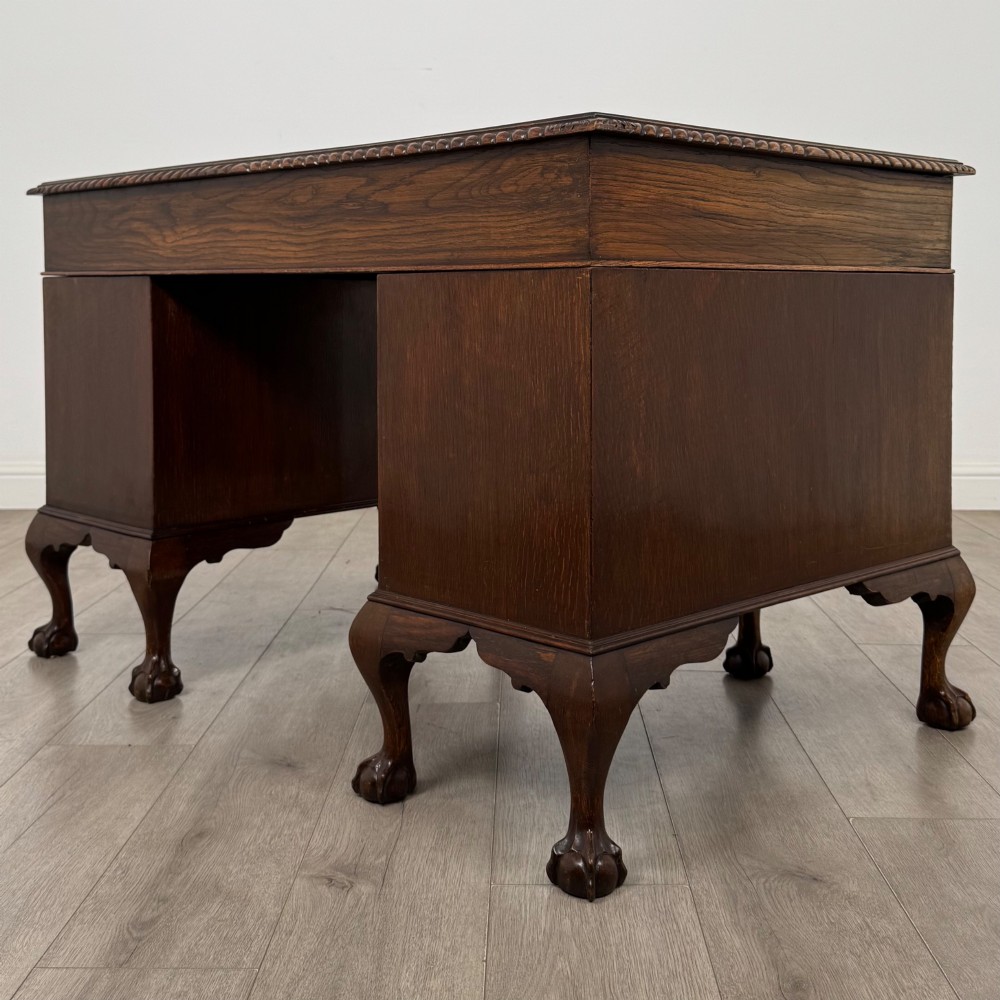 An antique oak pedestal desk featuring twin drawer pedestals, carved borders, and cabriole legs terminating in ball-and-claw feet. View VI