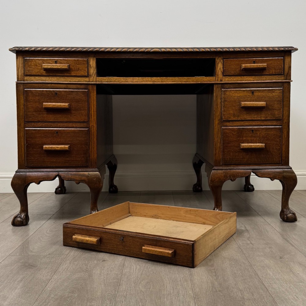 An antique oak pedestal desk featuring twin drawer pedestals, carved borders, and cabriole legs terminating in ball-and-claw feet. View X
