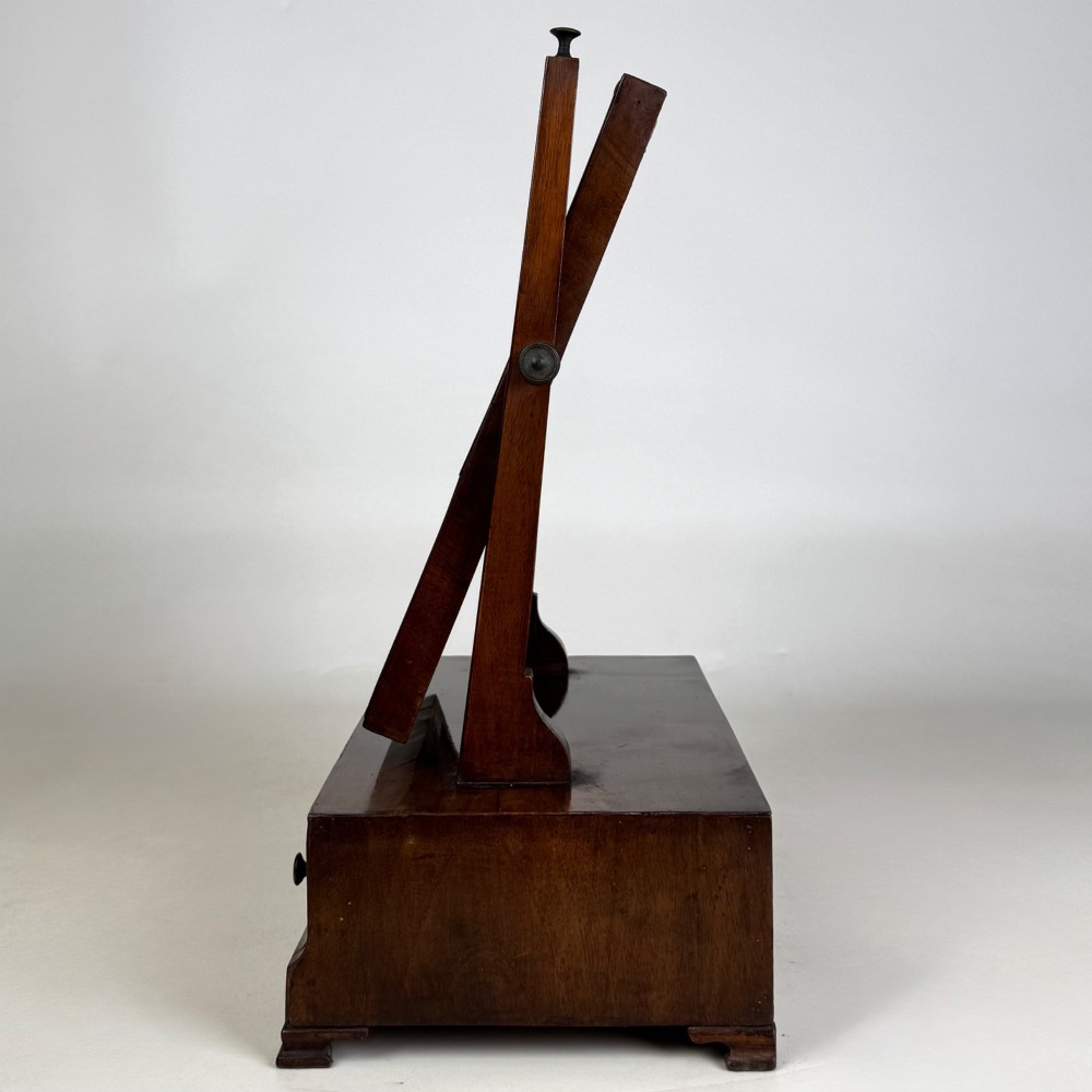 An 18th-century Georgian mahogany dressing mirror featuring an adjustable rectangular tilting glass plate supported above a shaped box base containing three small drawers. View II