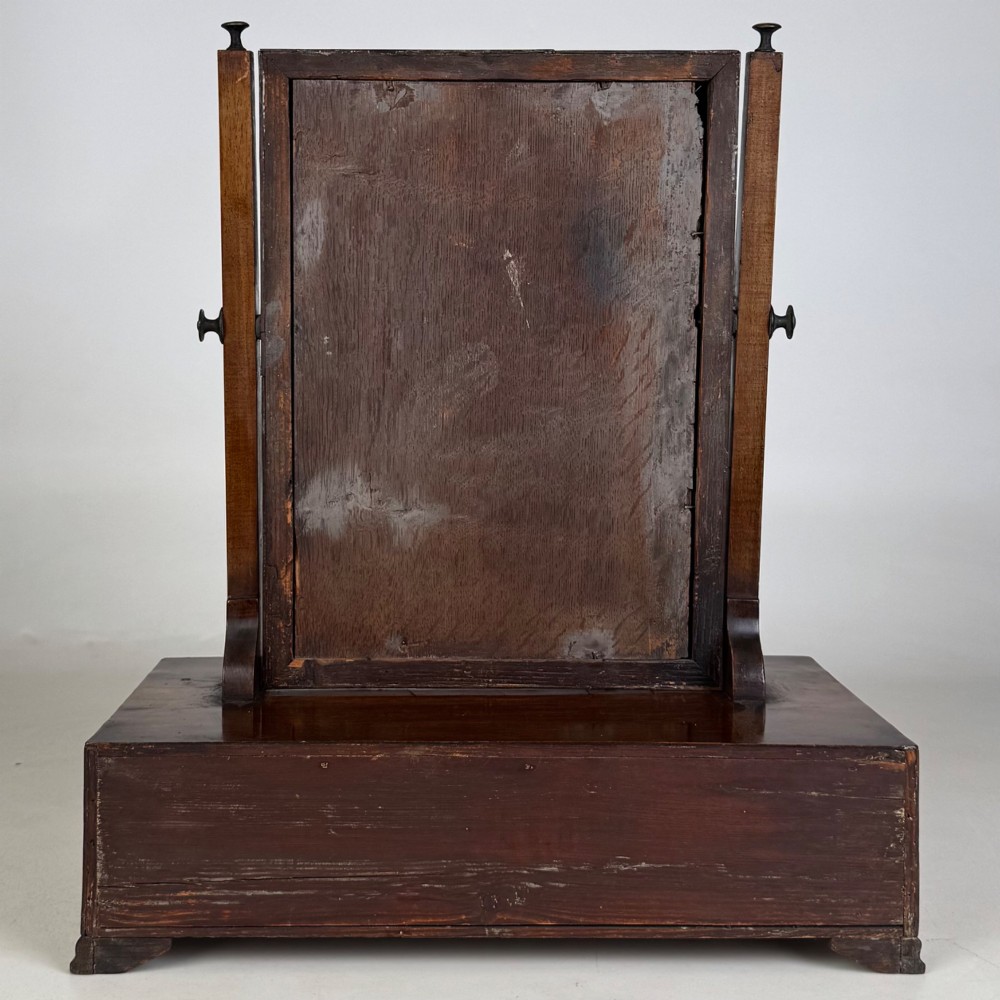 An 18th-century Georgian mahogany dressing mirror featuring an adjustable rectangular tilting glass plate supported above a shaped box base containing three small drawers. View V
