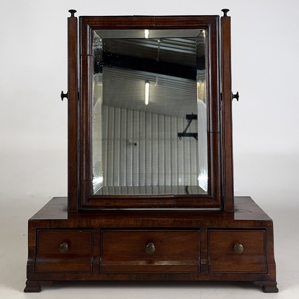 An 18th-century Georgian mahogany dressing mirror featuring an adjustable rectangular tilting glass plate supported above a shaped box base containing three small drawers. View X
