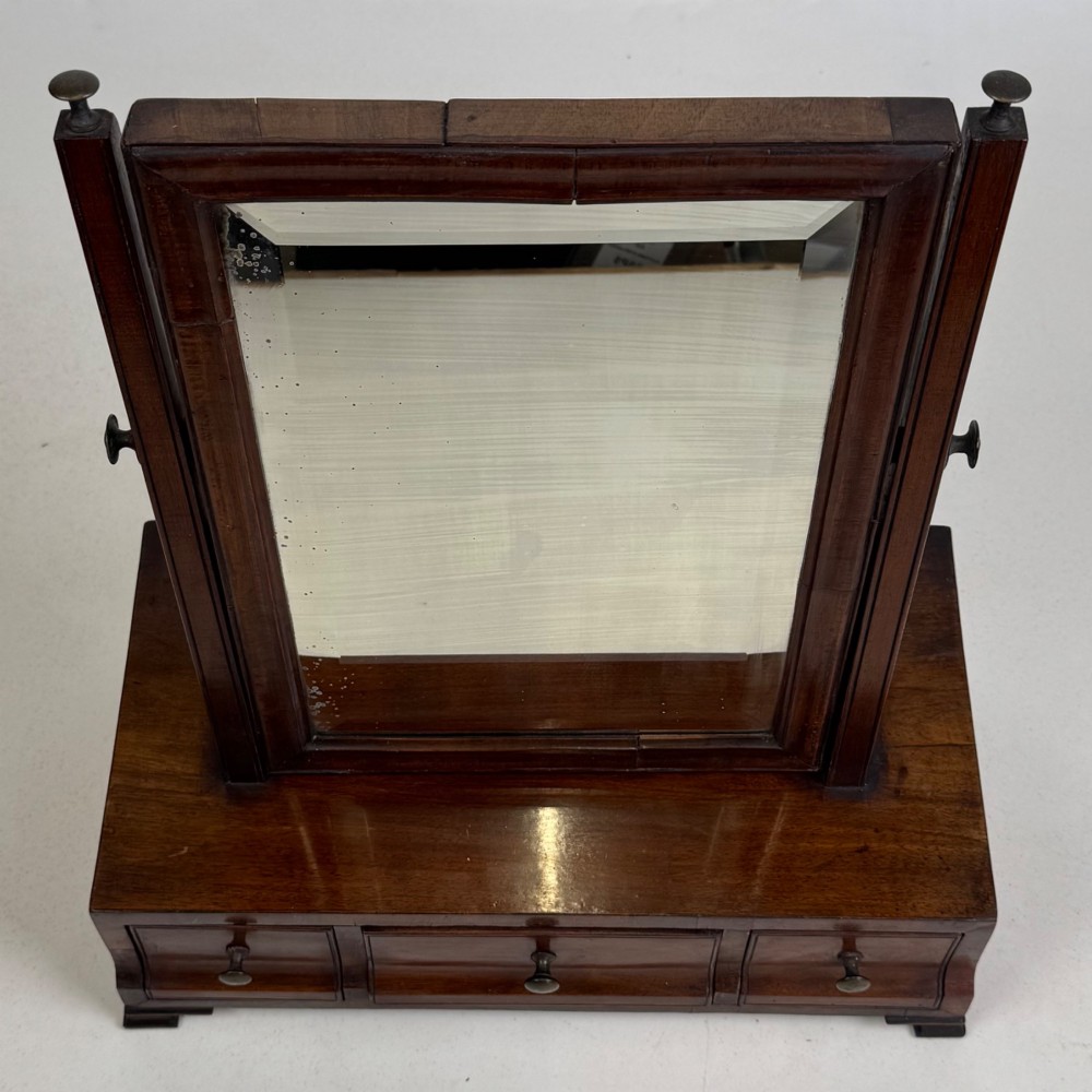 An 18th-century Georgian mahogany dressing mirror featuring an adjustable rectangular tilting glass plate supported above a shaped box base containing three small drawers. View XII