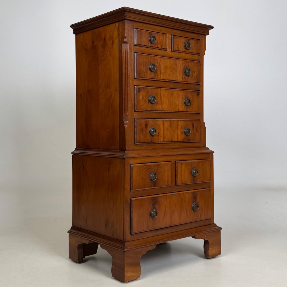 A small yew wood chest of drawers featuring a stepped tallboy structure with brass ring handles and bracket feet. View VIII