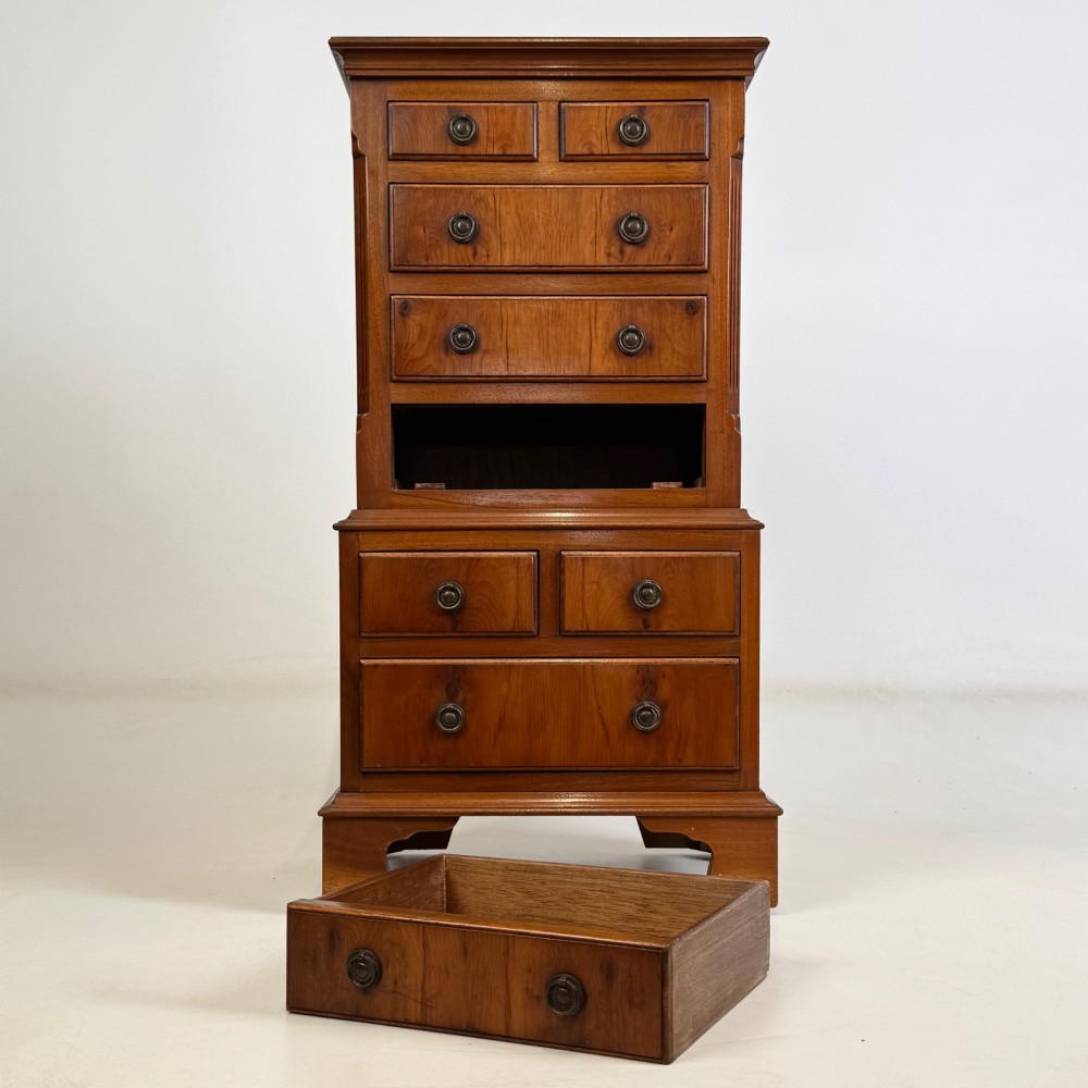 A small yew wood chest of drawers featuring a stepped tallboy structure with brass ring handles and bracket feet. View IX