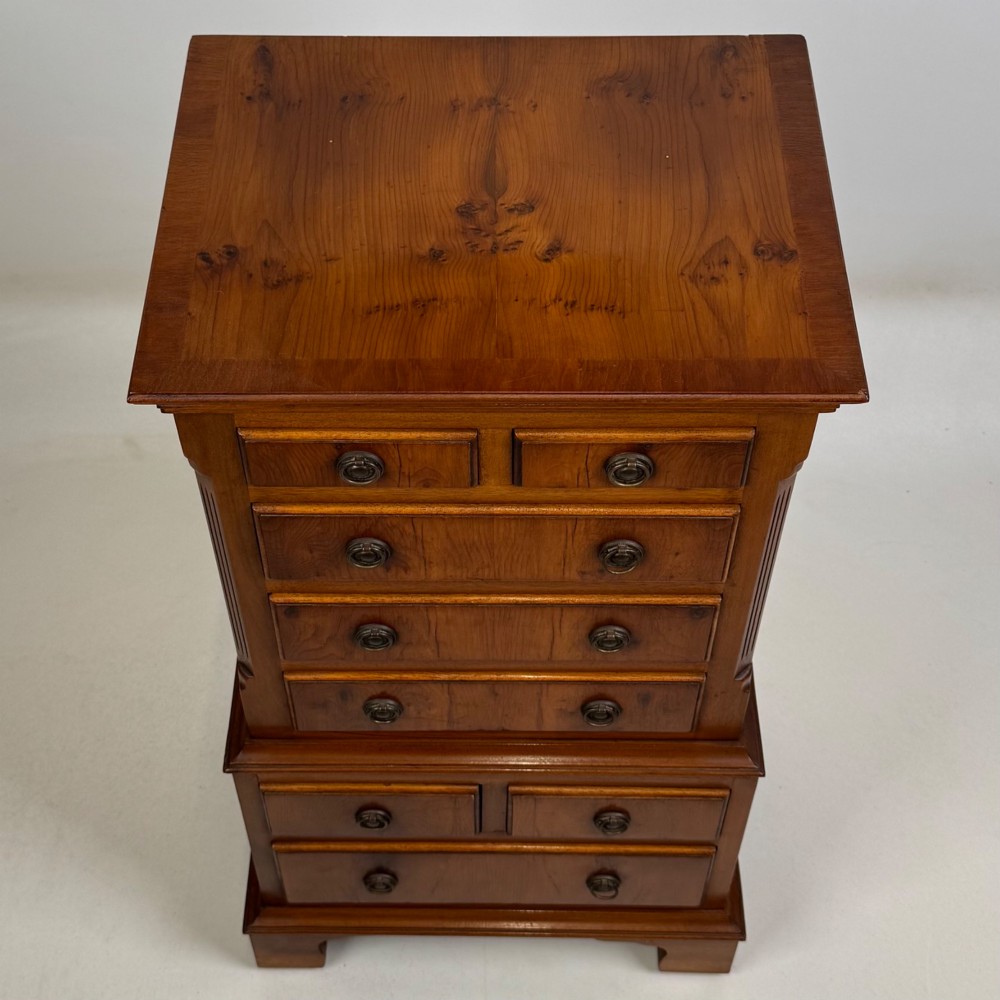 A small yew wood chest of drawers featuring a stepped tallboy structure with brass ring handles and bracket feet. View XI