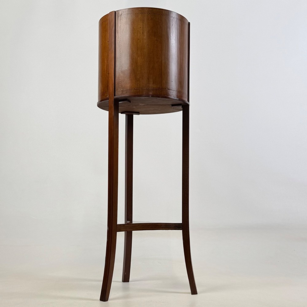 A tall Edwardian mahogany plant stand featuring a cylindrical top bucket with subtle line inlay, supported by three elongated curved legs and a triangular lower shelf. View IV