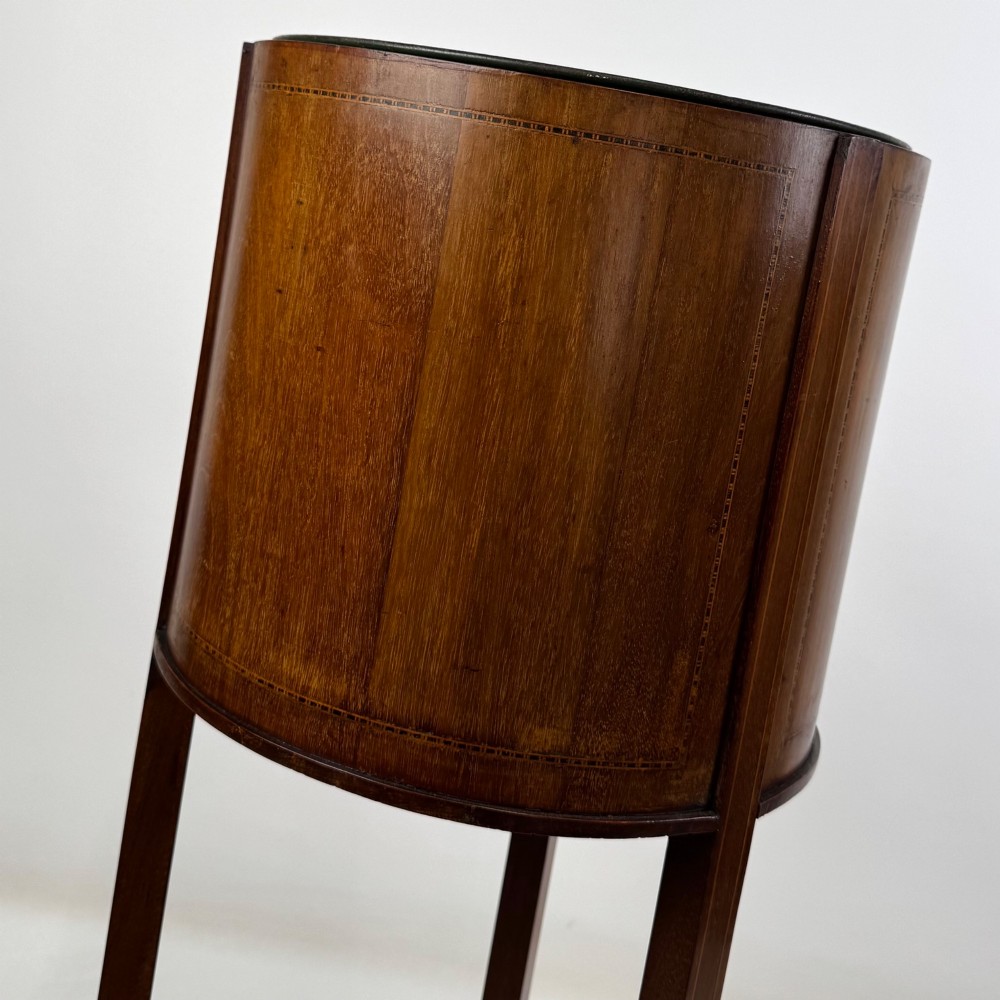 A tall Edwardian mahogany plant stand featuring a cylindrical top bucket with subtle line inlay, supported by three elongated curved legs and a triangular lower shelf. View VI