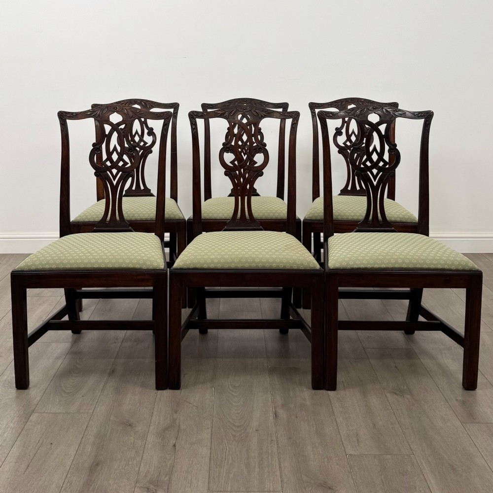 A set of six Georgian mahogany dining chairs featuring intricate carved pierced splat backs, square legs, and light green patterned upholstered seats.