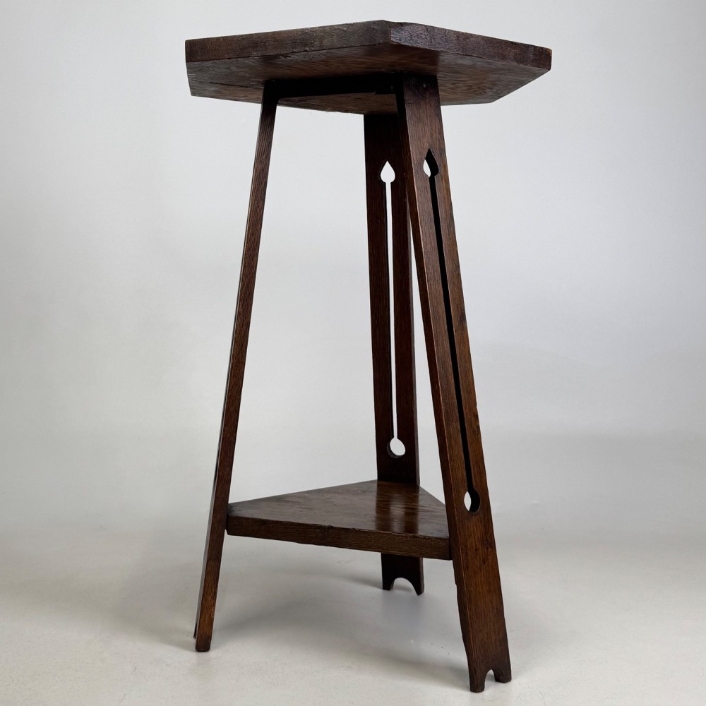 An antique dark oak Arts and Crafts side table featuring a hexagonal top, three splayed legs with pierced cutouts, and a lower triangular shelf. View II