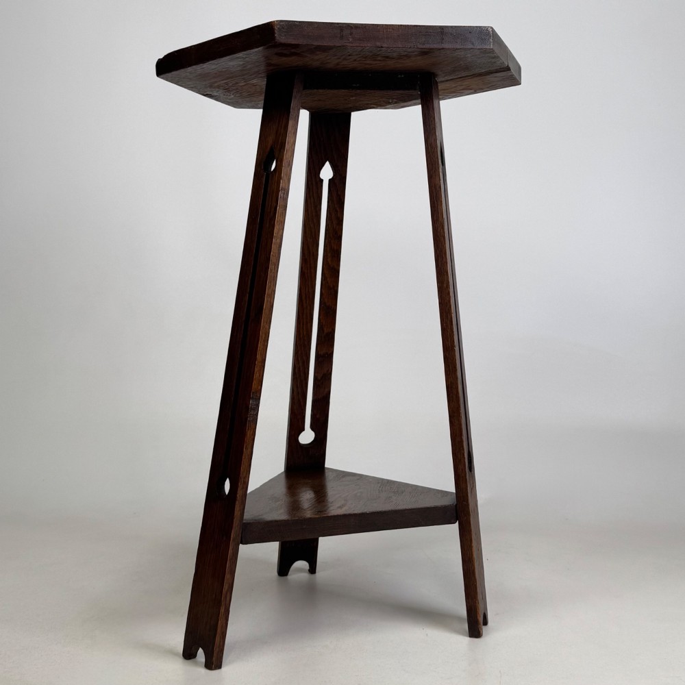 An antique dark oak Arts and Crafts side table featuring a hexagonal top, three splayed legs with pierced cutouts, and a lower triangular shelf. View IV