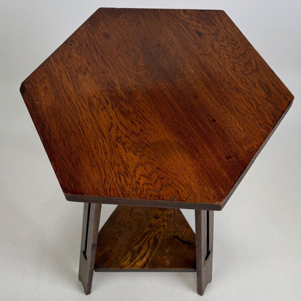 An antique dark oak Arts and Crafts side table featuring a hexagonal top, three splayed legs with pierced cutouts, and a lower triangular shelf. View V
