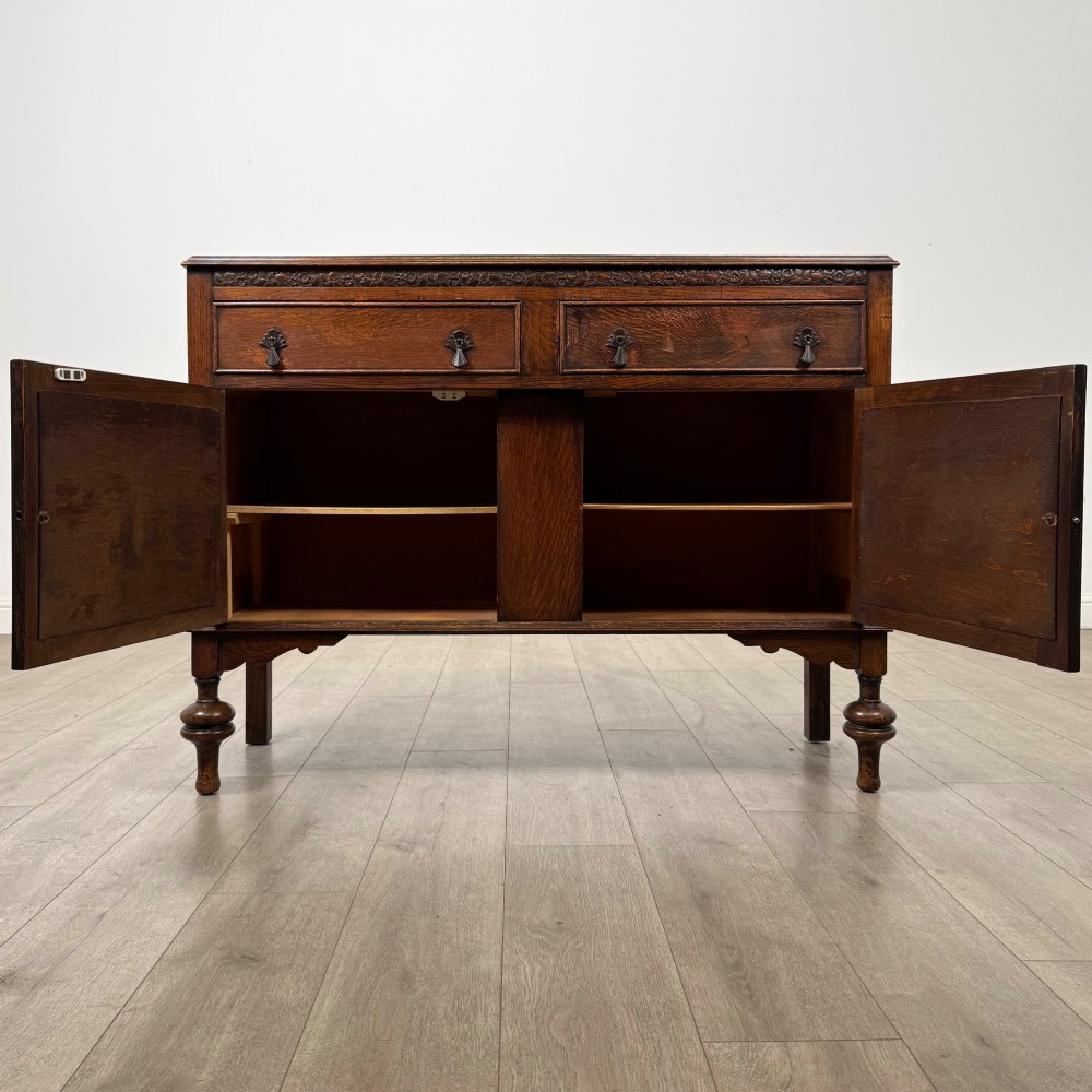 A dark oak sideboard featuring two carved drawers above a double-door cupboard resting on turned legs. View II