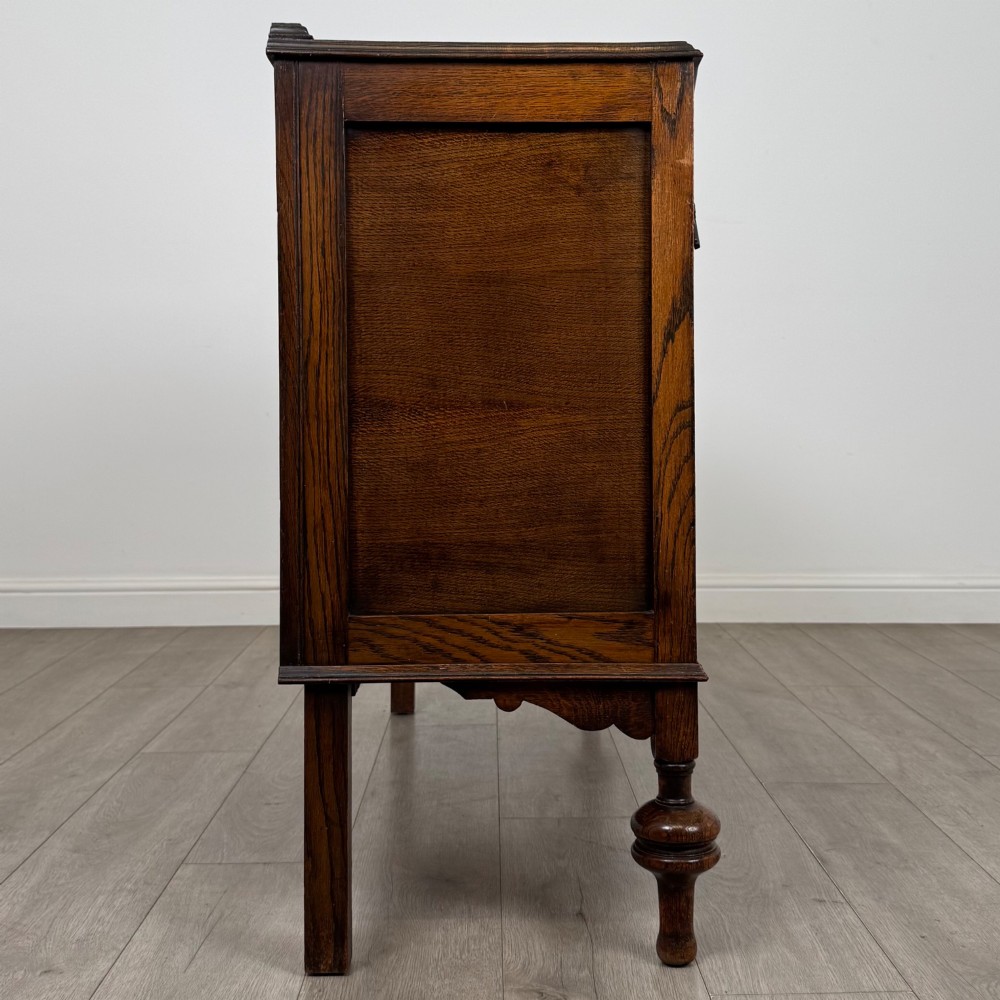 A dark oak sideboard featuring two carved drawers above a double-door cupboard resting on turned legs. View VIII