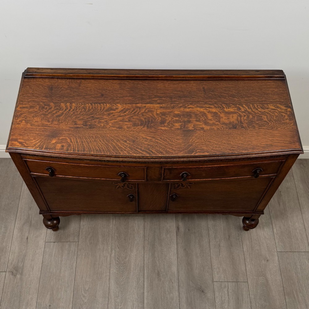 A dark oak sideboard featuring two carved drawers above a double-door cupboard resting on turned legs. View X