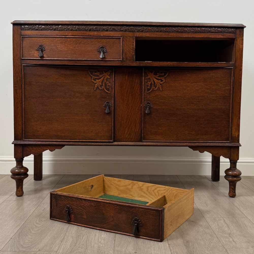 A dark oak sideboard featuring two carved drawers above a double-door cupboard resting on turned legs. View XI