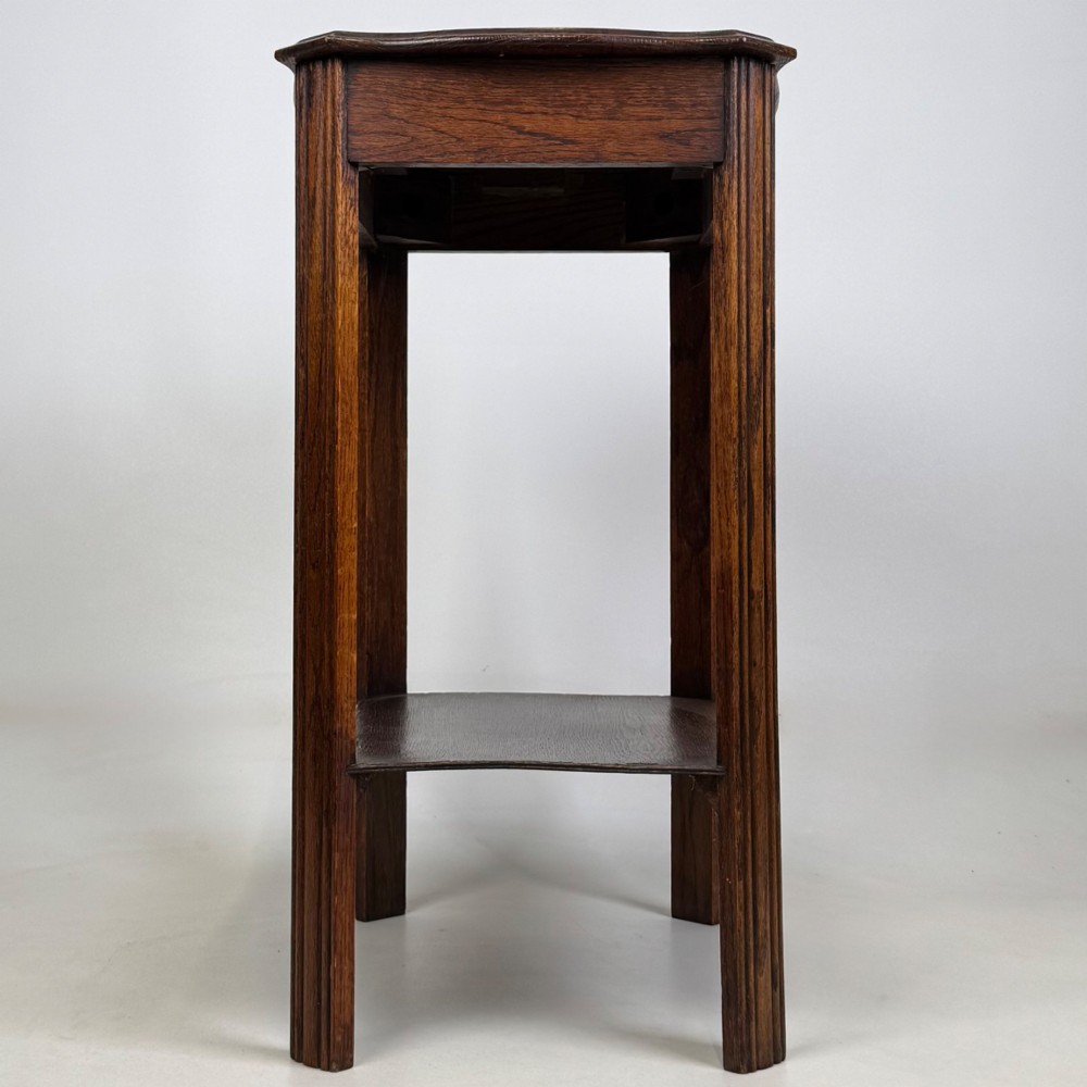 An Edwardian dark oak side table featuring fluted legs, a moulded top, and a lower shelf tier. View VII