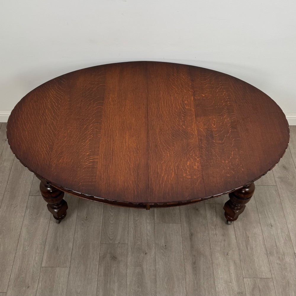 A large antique Edwardian extending oak dining table with detailed carved borders, thick turned legs, and brass castors. View VIII