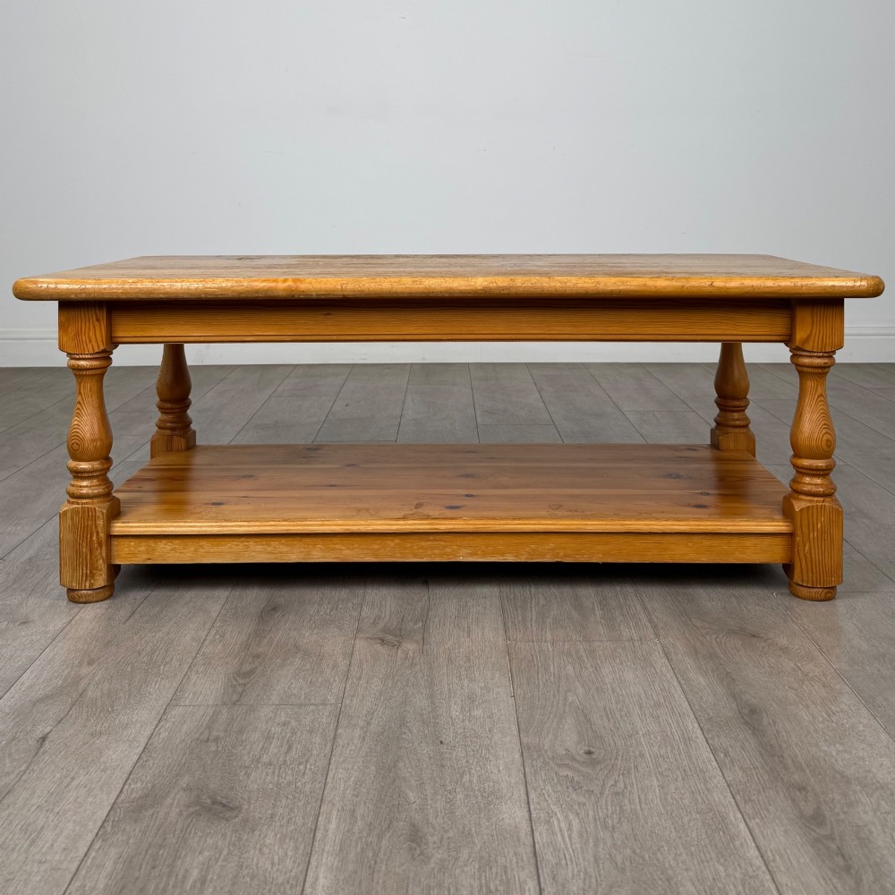 A rectangular warm pine coffee table featuring turned legs and a lower full-length storage shelf.