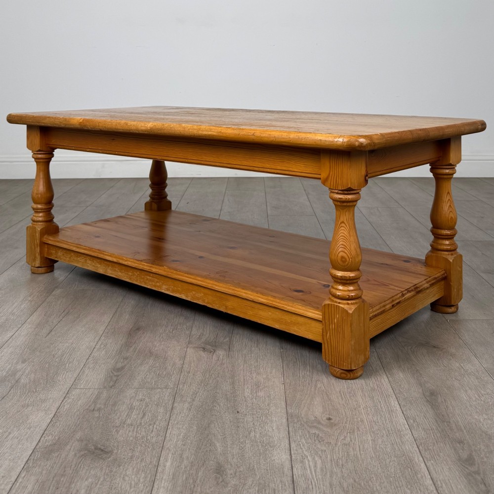 A rectangular warm pine coffee table featuring turned legs and a lower full-length storage shelf. View II