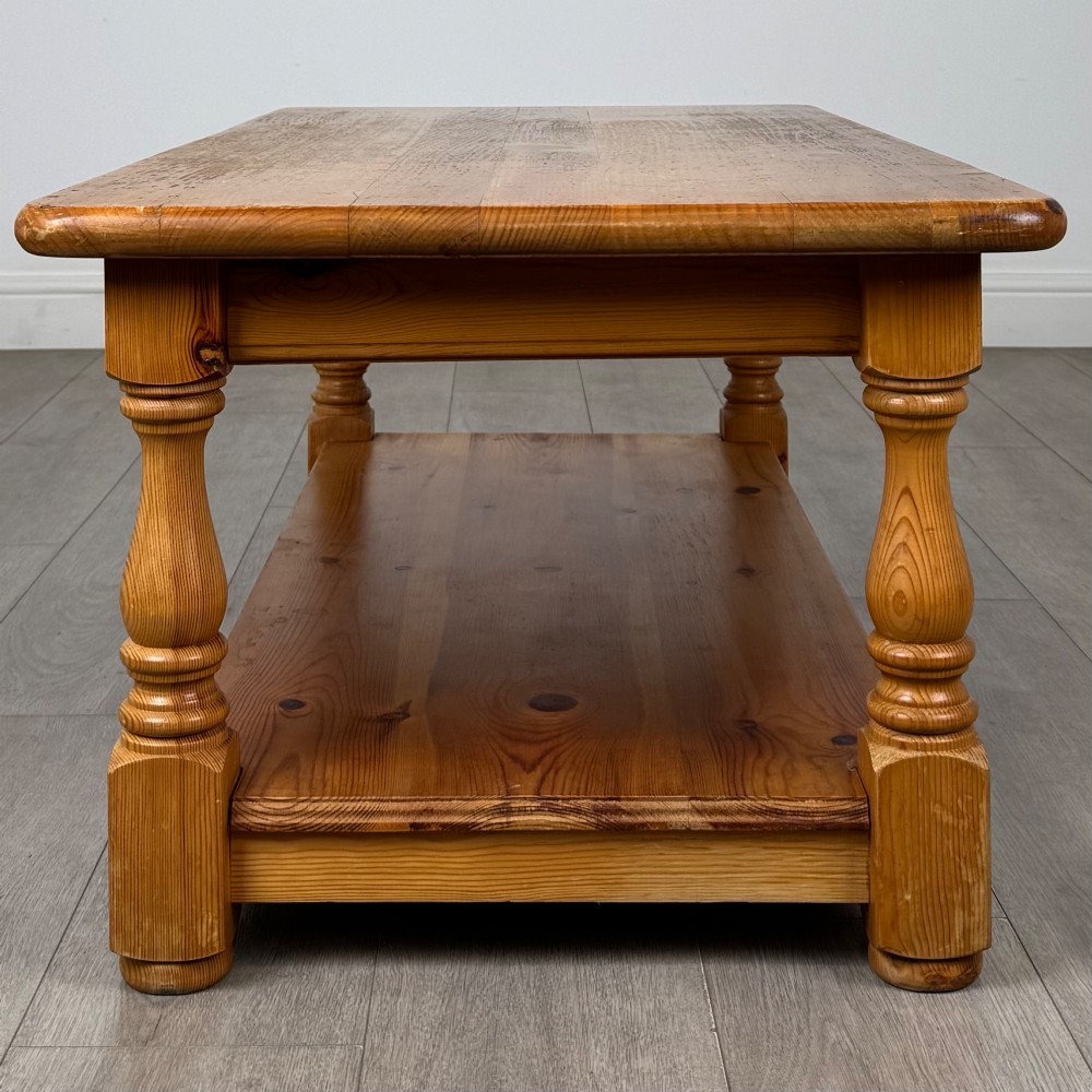 A rectangular warm pine coffee table featuring turned legs and a lower full-length storage shelf. View III