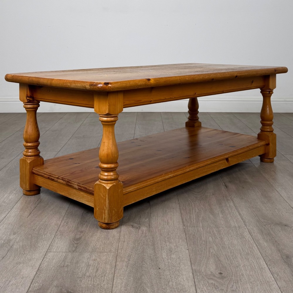A rectangular warm pine coffee table featuring turned legs and a lower full-length storage shelf. View IV