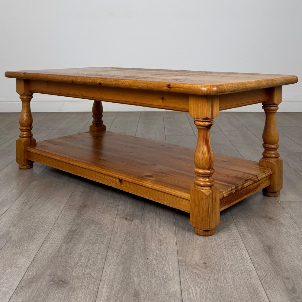 A rectangular warm pine coffee table featuring turned legs and a lower full-length storage shelf. View VI