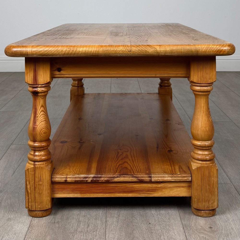 A rectangular warm pine coffee table featuring turned legs and a lower full-length storage shelf. View VII