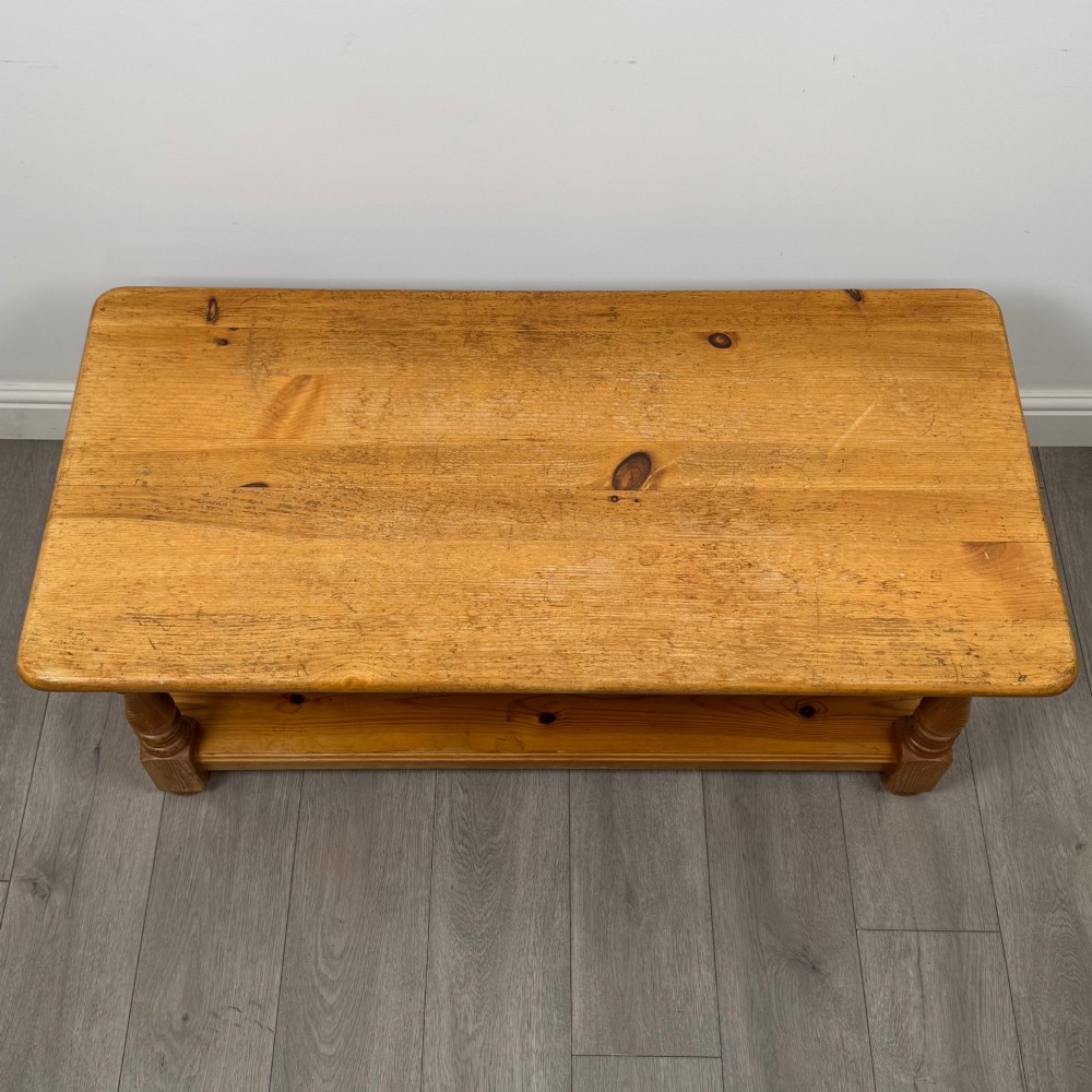 A rectangular warm pine coffee table featuring turned legs and a lower full-length storage shelf. View IX