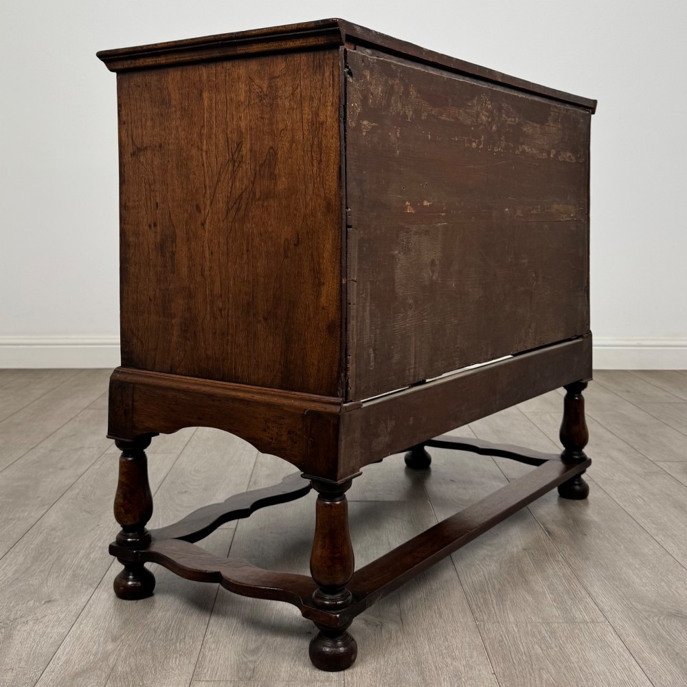 An antique 19th-century William and Mary style walnut chest of drawers featuring two deep drawers with ornate brass drop handles, raised on turned legs connected by a wavy stretcher base. View IV