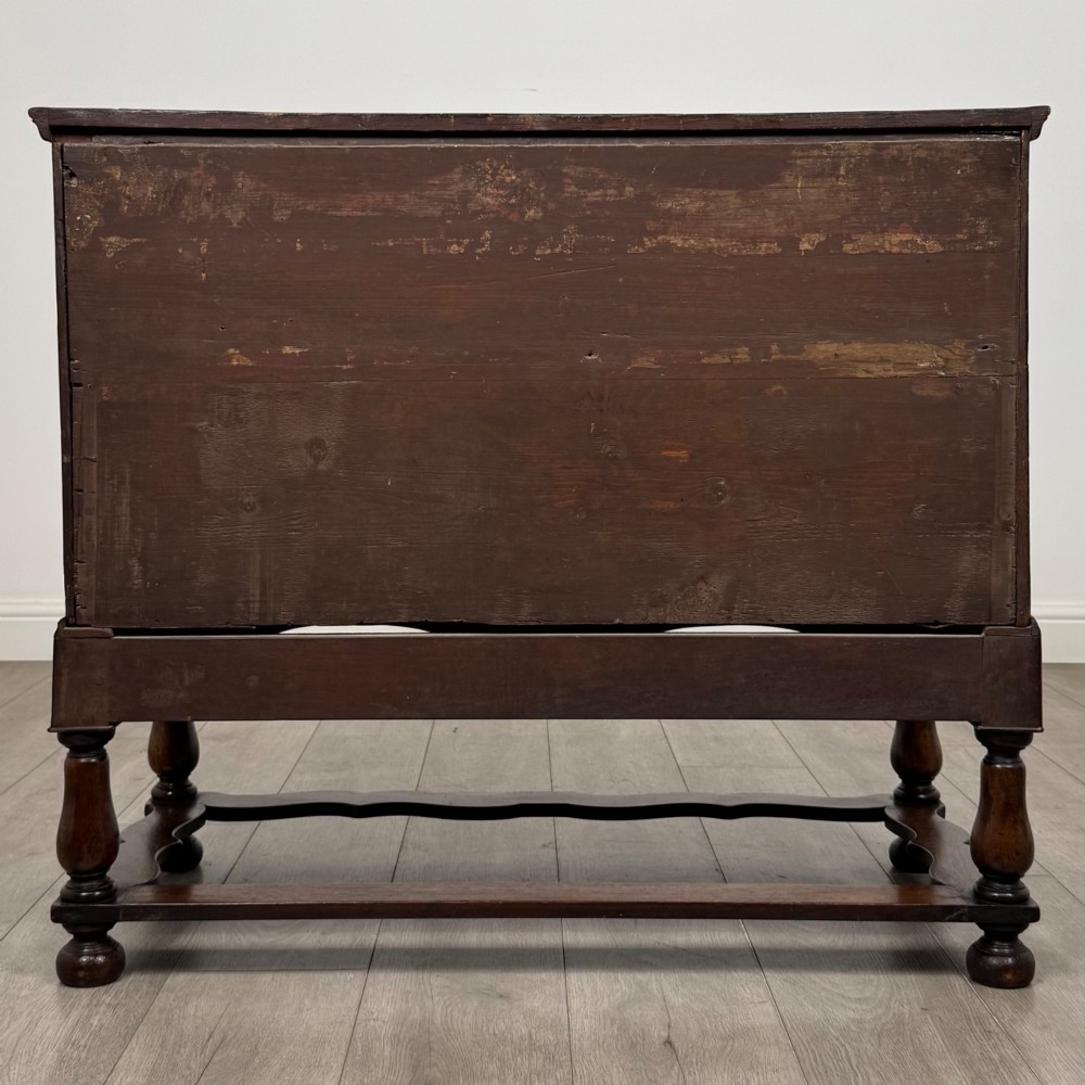 An antique 19th-century William and Mary style walnut chest of drawers featuring two deep drawers with ornate brass drop handles, raised on turned legs connected by a wavy stretcher base. View V