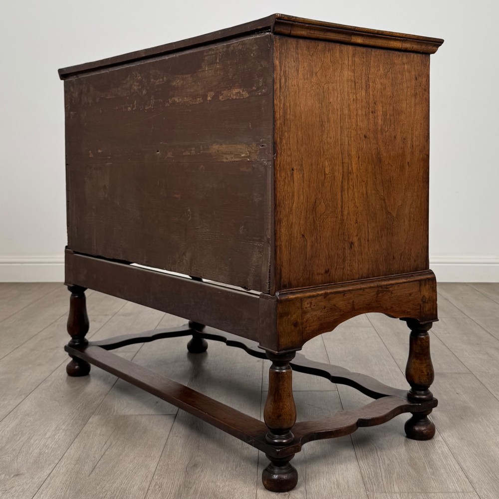 An antique 19th-century William and Mary style walnut chest of drawers featuring two deep drawers with ornate brass drop handles, raised on turned legs connected by a wavy stretcher base. View VI