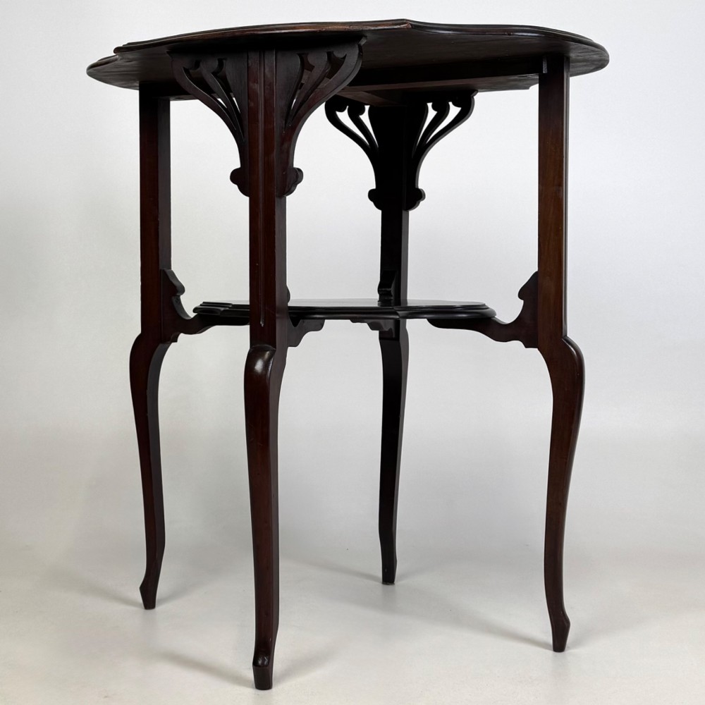 An Edwardian dark mahogany side table featuring a shaped top, pierced carved spandrels, slender cabriole legs, and a lower tier shelf.