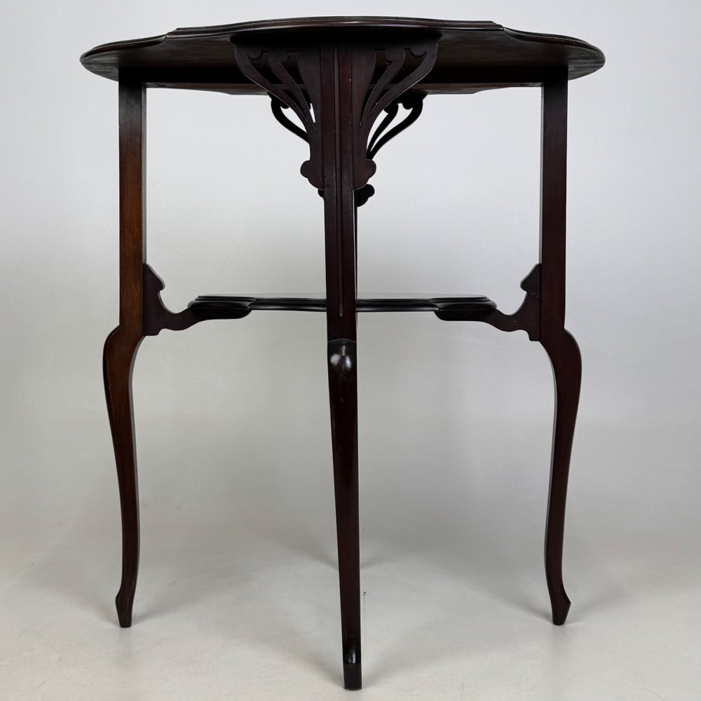 An Edwardian dark mahogany side table featuring a shaped top, pierced carved spandrels, slender cabriole legs, and a lower tier shelf. View IV