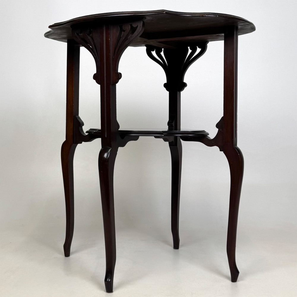 An Edwardian dark mahogany side table featuring a shaped top, pierced carved spandrels, slender cabriole legs, and a lower tier shelf. View V