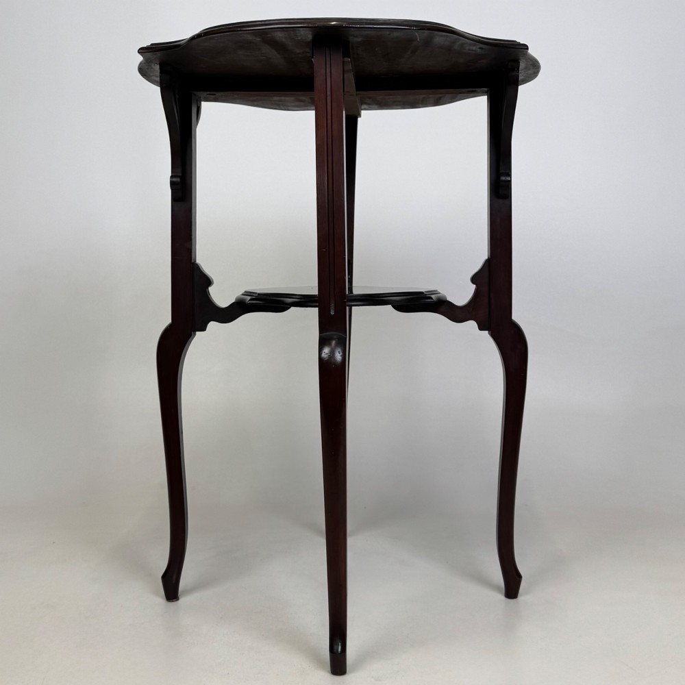 An Edwardian dark mahogany side table featuring a shaped top, pierced carved spandrels, slender cabriole legs, and a lower tier shelf. View VI